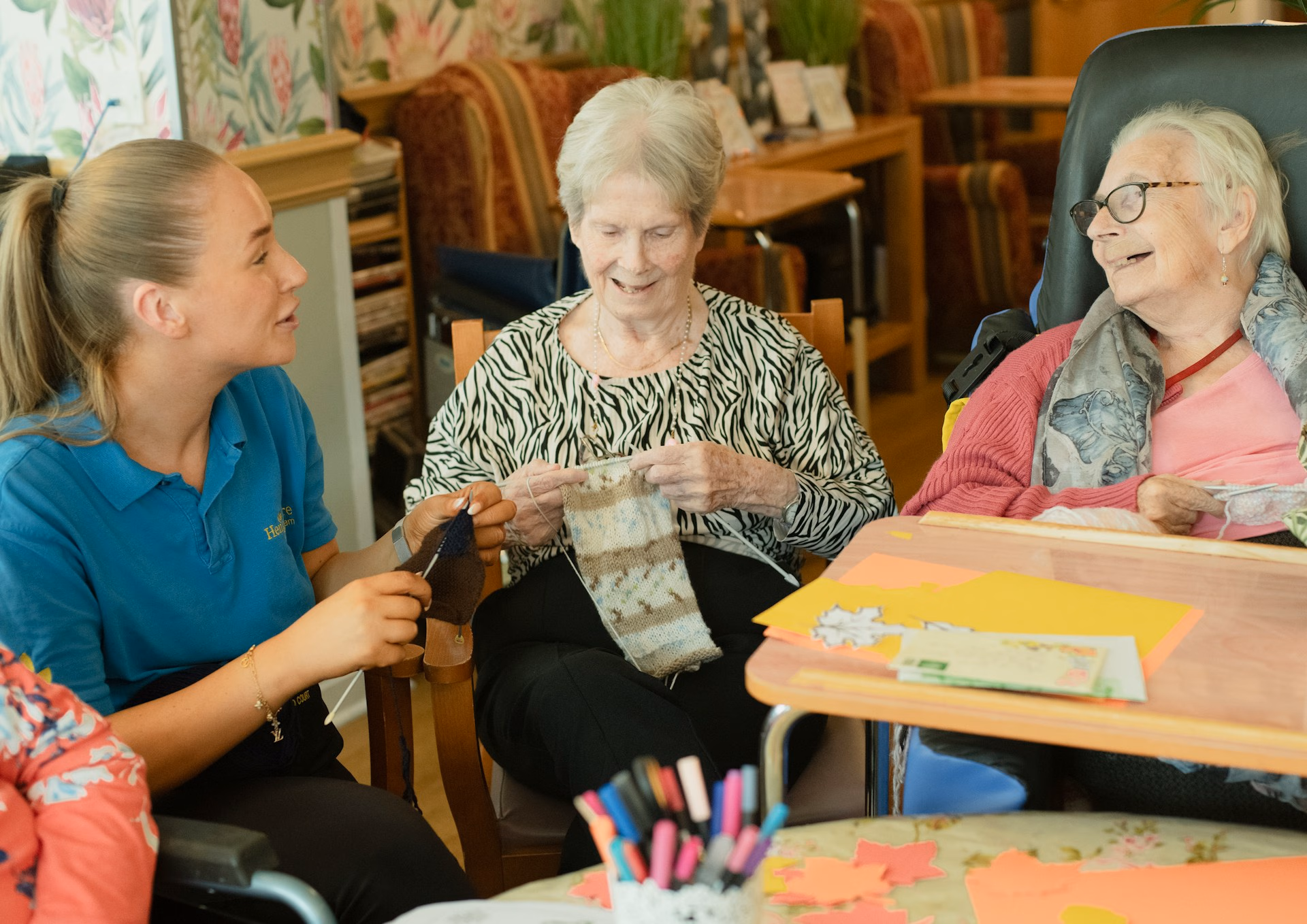 Three women sitting together knitting in a cozy room with craft supplies on the table.